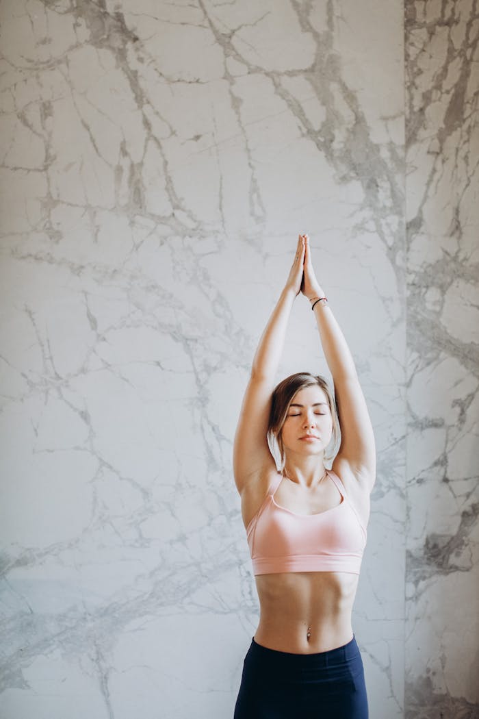 footer-cta-img Young woman performing upward salute yoga pose indoors with marble background.