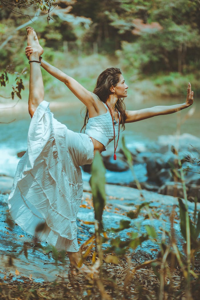 gallery-01 A serene scene of a woman practicing yoga by a picturesque river shore, embodying balance and tranquility.